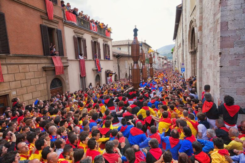 I tre grandi Ceri di legno portati a spalla di corsa dai ceraioli tra la folla nelle vie storiche di Gubbio
